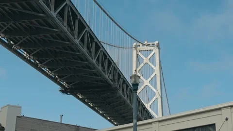 Suspension bridge tower and double deck span pass above historic building Video stock 342666292
