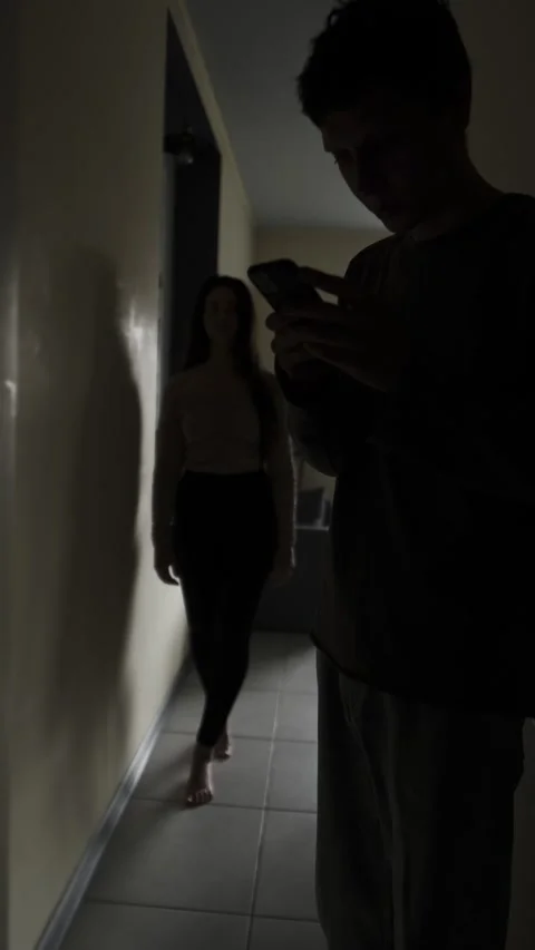 Suspicious boyfriend secretly texting while girlfriend watches in hallway Stock Footage 321689800