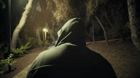 Suspicious hooded figure walks in a dark park at night,,gimbal tracking Stock Footage