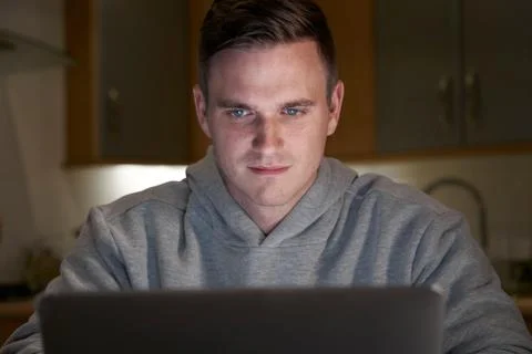 Suspicious Looking Man Using Laptop In Evening At Home Stock Photos
