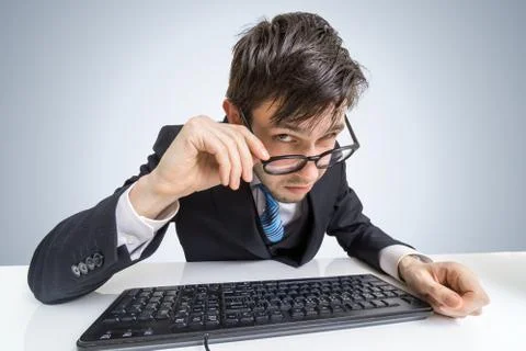 Suspicious man in glasses is working with computer and looking at you. Stock Photos