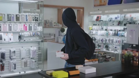 Suspicious man steals in a gadget store. The thief hides the goods and runs away Stock Footage 229548827