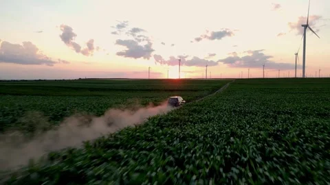 SUV Driving Through Fields with Wind Turbines in the Golden Hour Stock Footage 294690293