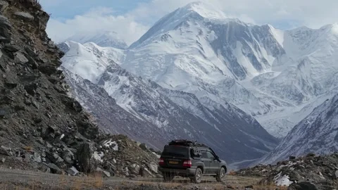 SUV navigating rugged mountain road with breathtaking snow-capped peaks Video stock 319538394