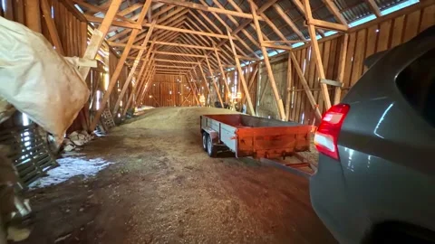 SUV towing a flatbed trailer inside a wooden farm barn with sawdust-covered Stock Footage 333318228