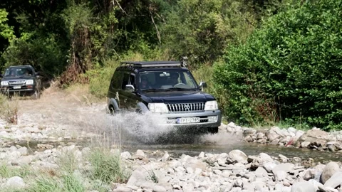 SUVs Navigating Rocky Stream in Forested Terrain Stock Footage 336315758