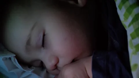 Swaddled 9 months baby boy sleeping in crib in evening in light of night lamp Stock Footage 255246696