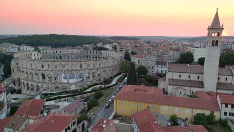 Swallows flying in front of a bell tower and Pula's Amphitheatre, pink sky Stock Footage 231329012