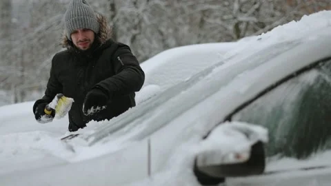 Swarthy man raises wiper blades and brushes snow from windshield of car. Stock-Footage 227197604