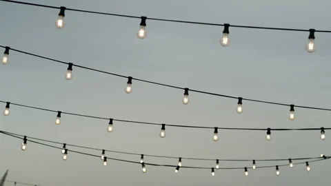 Swaying Garden String Lights in the Wind Against Overcast sunset Sky Stock Footage 321430283