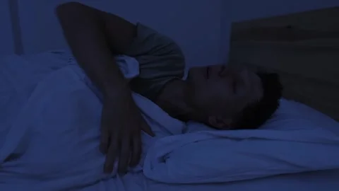 Sweating man tossing in bed and throwing off covers to cool down, unable to Stock Footage 346251299