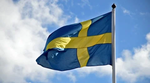 A Swedish flag flutters in the wind against a blue sky background Stock Footage 65730891
