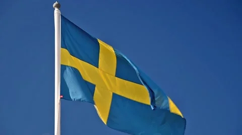 A Swedish flag flutters in the wind against a blue sky background Stock Footage 65730904