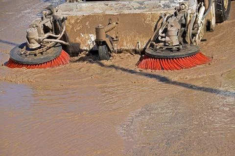 Sweeper machine digs its brushes into the mud of the street, to drag away a.. Stock Photos
