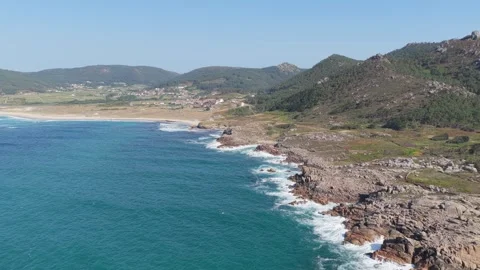A sweeping aerial shot captures the dramatic rocky coastline and expansive sandy Stock Footage 346717371