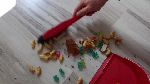 Sweeping up spilled snacks hand uses red brush and dustpan to clean colorful gum Stock Footage 312198163