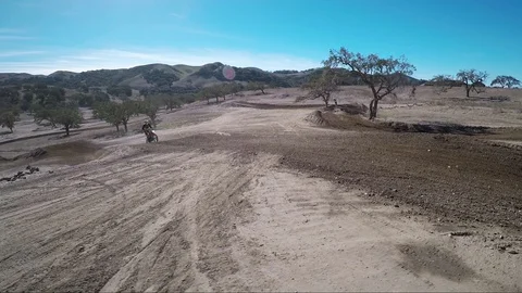Sweeping view of bikers doing jumps on a hilly desert race track course Video stock 92108015