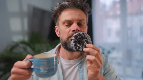 Sweet addiction concept. A man eats a donut and drinks coffee. Video stock 343448173