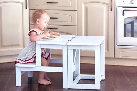 Sweet Baby Eats by herself at a Small Folding Ladder-Table Chair. Stock Photos