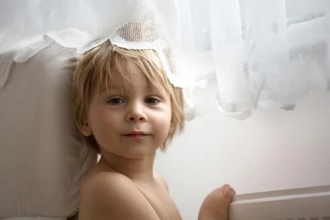 Sweet blond toddler child, boy, hiding behind the curtain at home Stock Photos