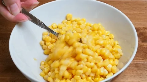 Sweet canned corn is mixed into a ceramic bowl for making salad. 動画素材 346801816
