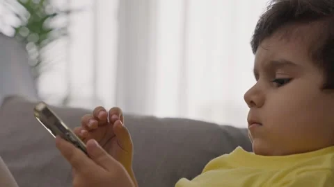 Sweet child sitting on sofa concentrated on electronic application on cellphone Video stock 246322743