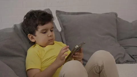 Sweet child sitting on sofa concentrated on electronic application on cellphone Stock Footage 248808051
