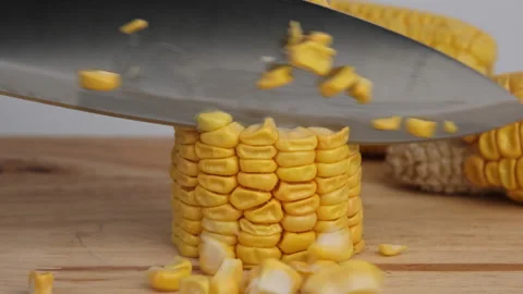 Sweet corn kernels are cut from the cob on a wooden cutting board with a knife. Stock Footage 243629943