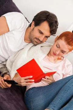 Sweet Couple Resting on Couch While Reading a Book Stock Photos