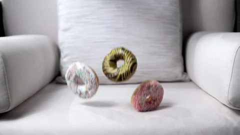 Sweet donuts in slow motion fall on a clean, white upholstered chair Stock Footage 191001645