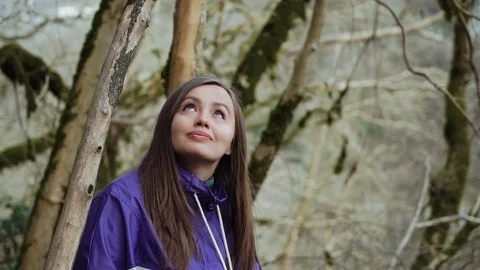 A sweet girl in a colored jacket is looking at the moss-covered trees in the 库存影片 113674849