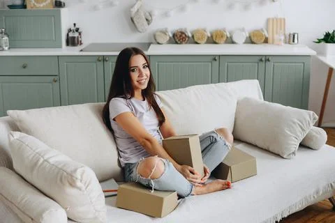 Sweet girl sits on couch with boxes. Freelancer Girl Working from Home. Cozy  Stock Photos