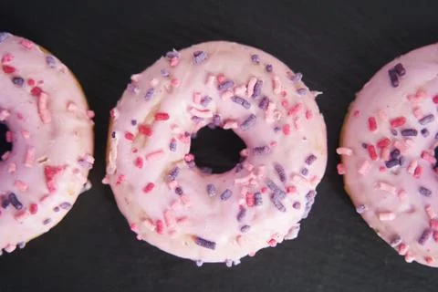 Sweet glazed pink donuts close-up on a black tray. Stock Photos