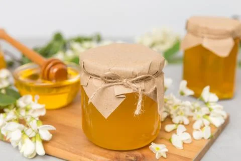 Sweet honey jar surrounded spring acacia blossoms. Honey flows from a spoon i Stock Photos