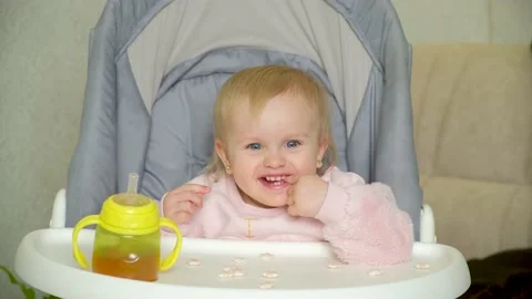 A sweet one-and-a-half-year-old girl sits in a high baby feeding chair and eats Stock Footage 228732009