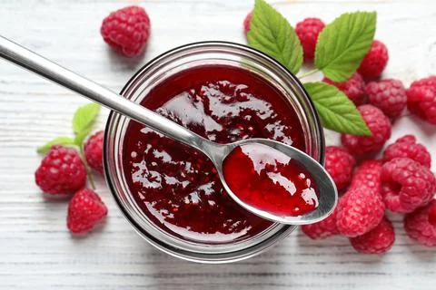 Sweet raspberry jam and fresh berries on white wooden table, flat lay Foto stock