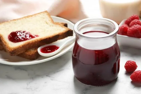 Sweet raspberry jam and toasts for breakfast on white marble table Stock Photos