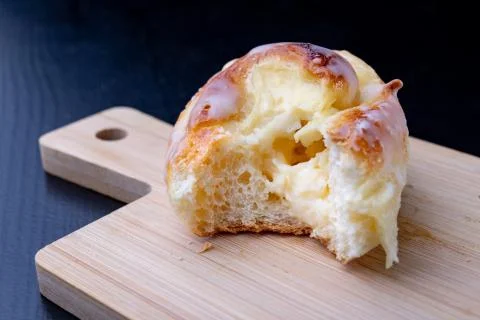 Sweet roll with icing on a small board. Tasty dessert on the kitchen table. Stock Photos