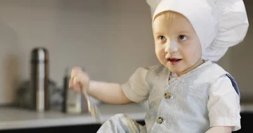A sweet small chef cook in a white culinary cap mixes the flour with a metal spo Stock Footage 85807685