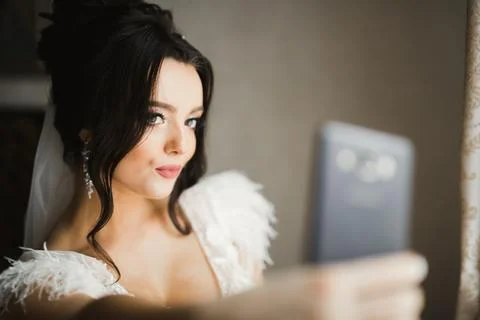 A sweet smiling bride in a light interior makes selfie on the phone Stock Photos