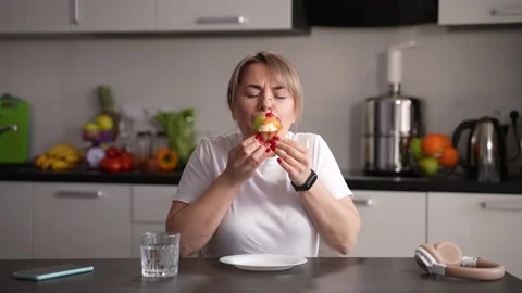 Sweet tooth female eating cupcake in kitchen Stock Footage 153471653