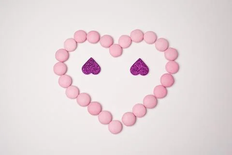 Sweets candies as heart with two glittering lilac hearts on white background. Stock Photos