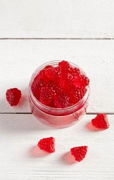Sweets in the shape of raspberry in a glass jar. White wooden background. Stock Photos