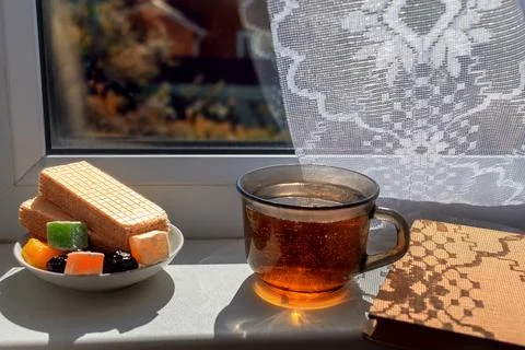 Sweets, tea and book by window in fall. Hard light with patterned shadows f.. Stock Photos