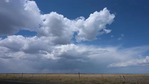 Swelling white puffy clouds with storm clouds in the distance above a field Stock Footage 154307193