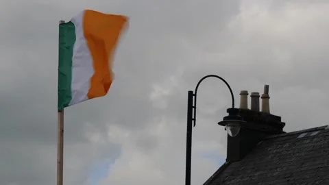 Swift Irish Flag Dance Amidst Cloudy Sky and Traditional Rooftop Stock Footage 259398218