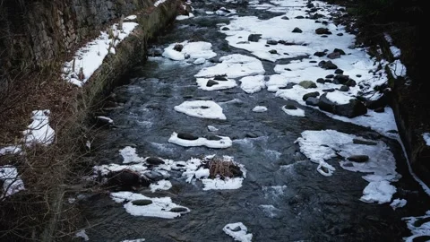 A swift river moves through a winter setting, with snow resting on the water and Stock Footage 303486282