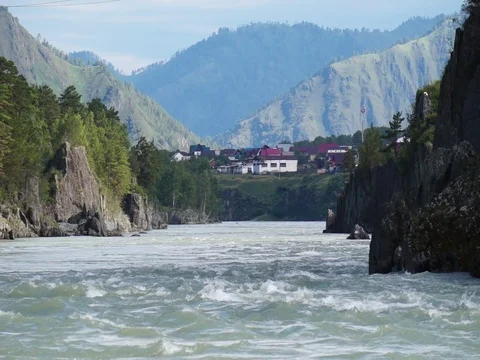 Swift water flow in mountain river with small village in background Stock Footage 76642101