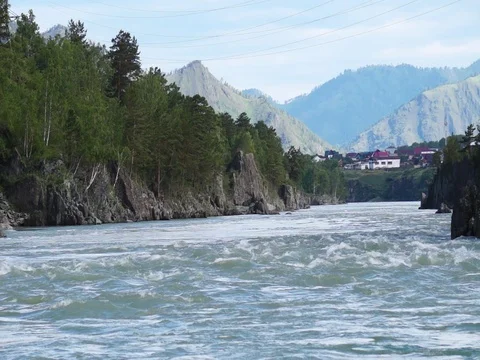 Swift water flow in mountain river with small village in background Stock Footage 76642204