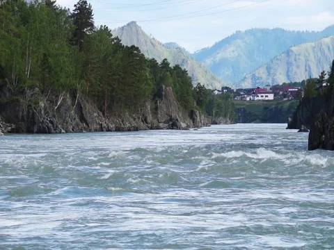 Swift water flow in mountain river with small village in background Stock Footage 76642344